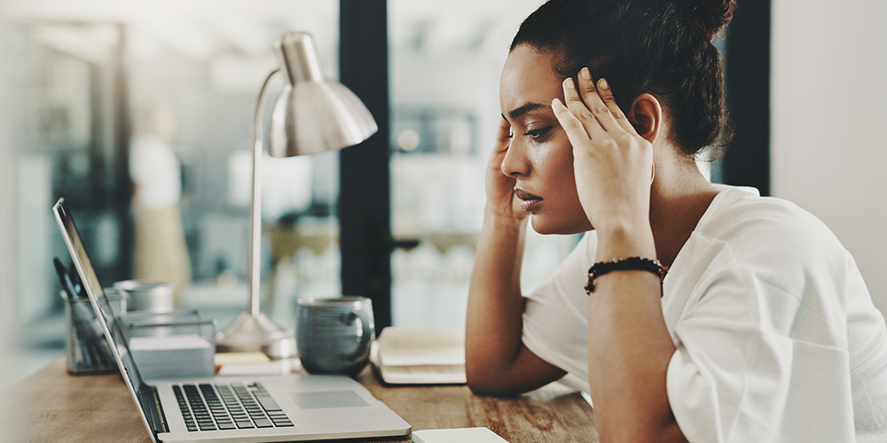 Woman sits at desk with fingers on her temples.