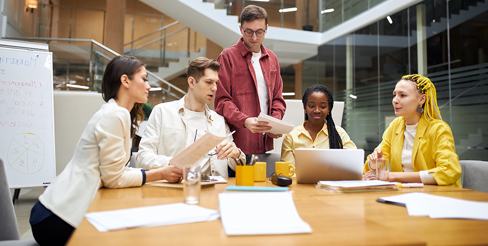 Five employees sit around a table discussing a project