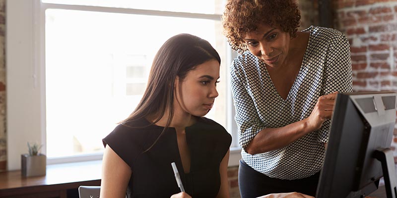 Two businesswoman in an office working together on a computer.