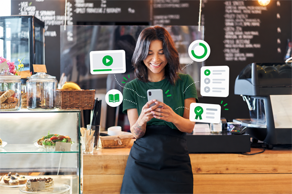 give me alt text for seo please Smiling café employee completing e-learning on a smartphone with floating course, progress, and completion icons